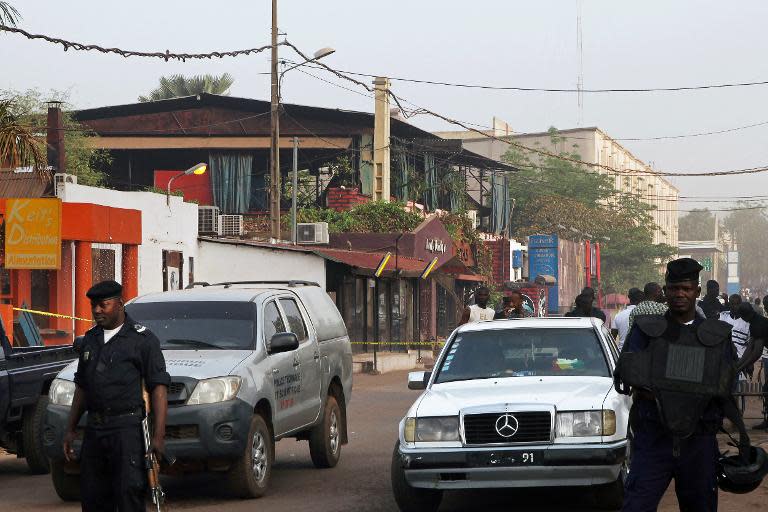 Policemen stand near the La Terrasse restaurant -- seen in the backround with the blue curtains -- in Bamako on March 7, 2015 after five people were shot dead overnight in a the restaurant in a suspected terror attack