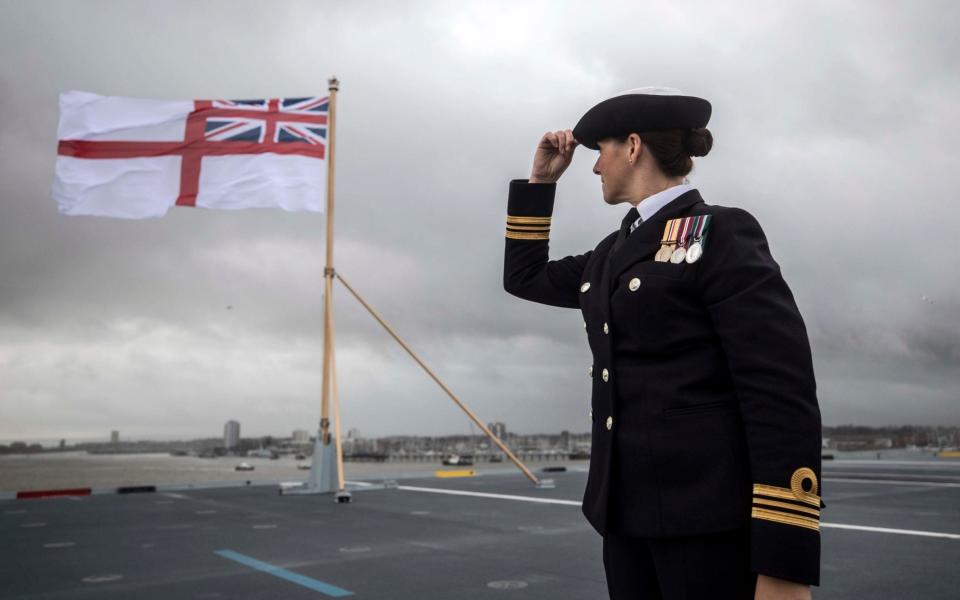 A naval officer looks up at the White ensign flag flying at the stern of the ship 