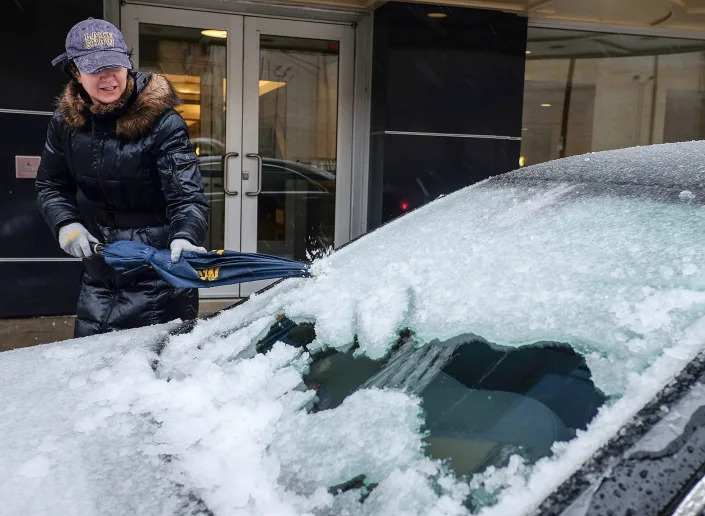 A woman uses an umbrella to chip away at the ice accumulation on her windshield in downtown Lansing, Mich. on April 15, 2018. Freezing rain that began falling overnight had left roads treacherous and cut power to hundreds of thousands of homes and businesses by midday Sunday in Michigan even as heavy snow was forecast to dump a foot or more of snow on parts of the state's Upper Peninsula by early Monday. 