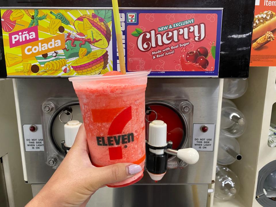 A hand filling up a large 7/11 cup with new and exclusive cherry slurpee