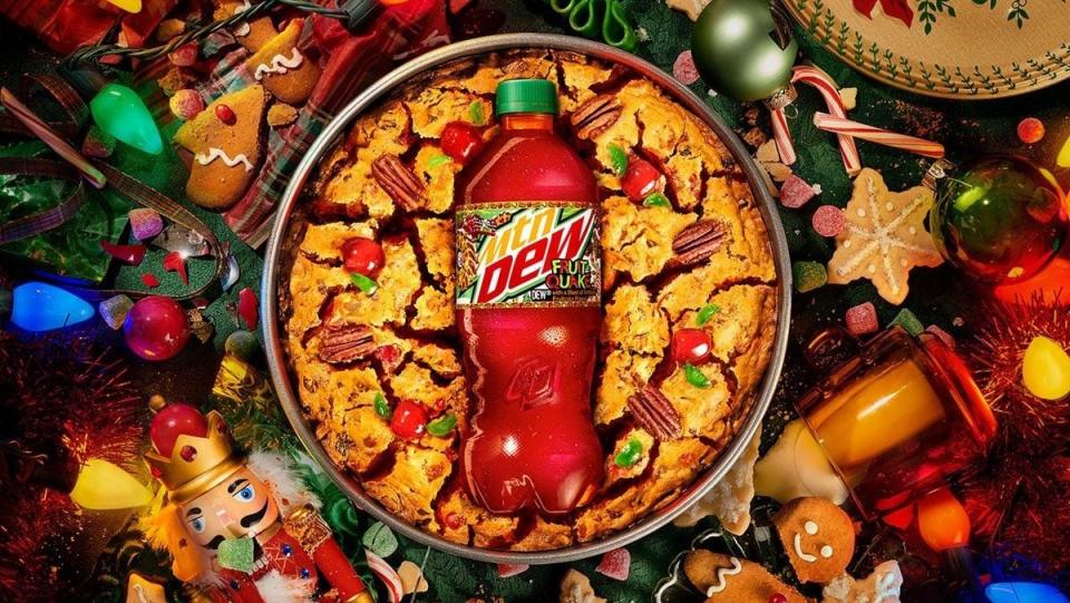 A bottle of MNT DEW Fruit Quake inside a fruitcake on a table of Christmas decor