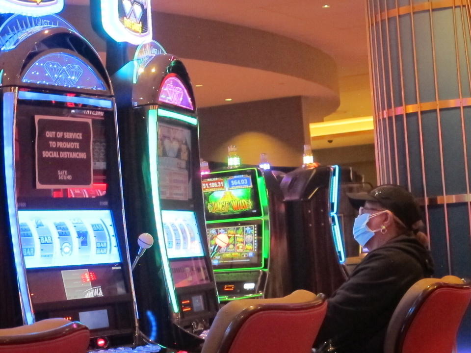 This May 3, 2021 photo shows an intentionally disabled slot machine next to a man playing a different slot machine while wearing a face mask at the Hard Rock casino in Atlantic City, N.J. On May 24, 2021, New Jersey gambling regulators released figures showing that the Atlantic City casinos' first quarter earnings more than tripled this year compared to the same period last year, when the COVID19 pandemic wiped out half of March. (AP Photo/Wayne Parry)