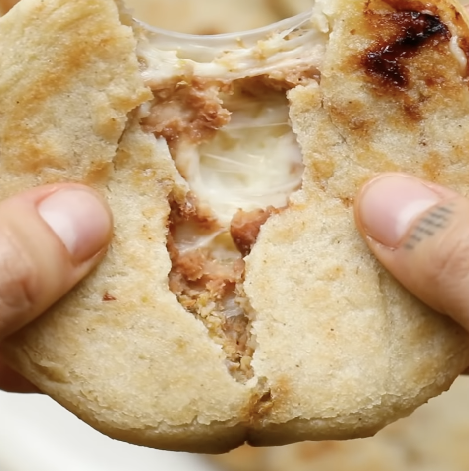 A person pulls apart a pupusa