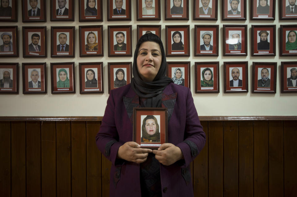 In this Wednesday, March 26, 2014 photo, Afghan lawmaker Samia Azizi Sadat from Parwan holds her picture which hangs on the wall among Afghanistan’s 249 parliamentarians in the parliament in Kabul, Afghanistan. In the last elections in 2010, 69 women won seats in Afghanistan’s 249-seat parliament. The next parliamentary vote will be held in 2015, but first are the April 5 presidential and provincial council elections. (AP Photo/Anja Niedringhaus)