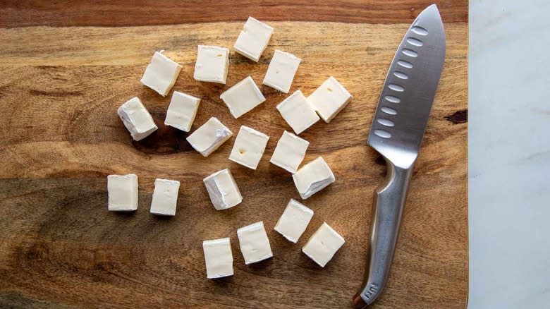 chopped up chunks of brie with knife on cutting board