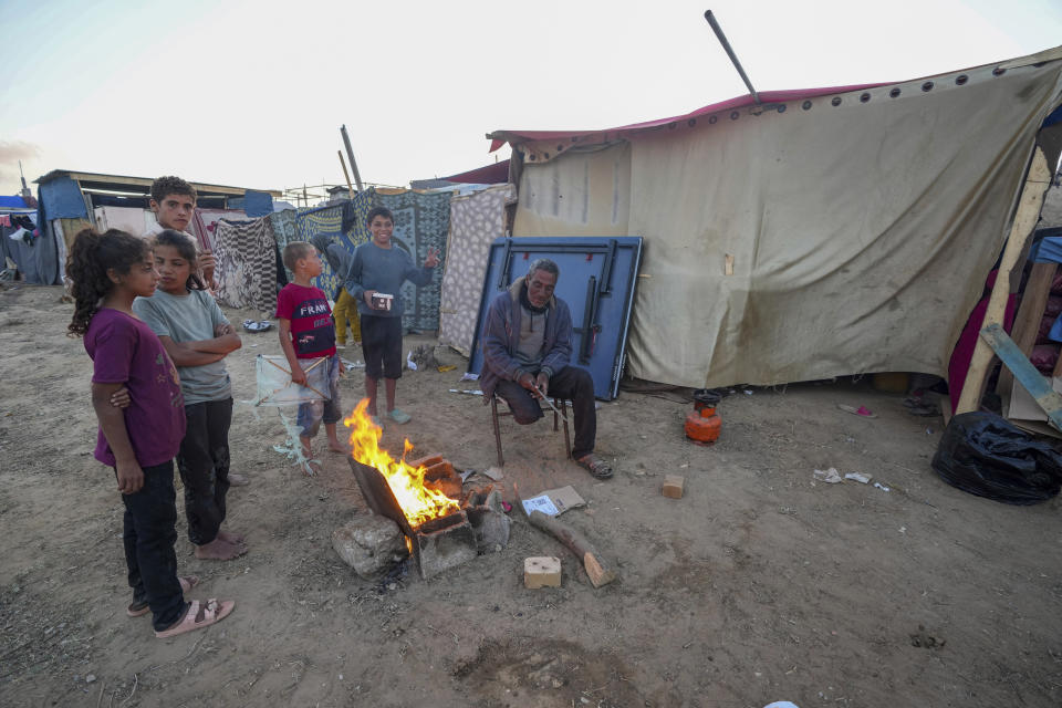 Un hombre palestino se sienta junto a una hoguera al lado de varios niños ante varias carpas improvisadas tras verse desplazados por la ofensiva aérea y terrestre israelí en la Franja de Gaza, en un campamento en Deir al Balah, el lunes 13 de mayo de 2024. Los palestinos conmemoraban el miércoles el 76to año desde su expulsión masiva de lo que ahora es Israel, un suceso en torno al que gira su lucha nacional. Pero en muchos aspectos, esa experiencia palidece en comparación con la calamidad que se produce ahora en Gaza. (AP Foto/Abdel Kareem Hana)