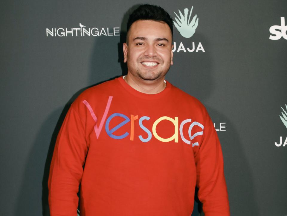 frankie delgado wearing a red sweatshirt that reads "versace," standing on a red carpet