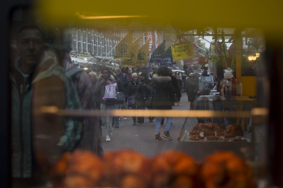 This March 20, 2013 photo shows people through and reflected in a stand with grilled chickens at Albert Cuyp market, Amsterdam, Netherlands. Amsterdam's wealth began in its port with the merchants who bought and sold everything from tulip bulbs to spices from the East Indies. A little of that mercantile past can still be seen at the city's many markets. The most famous is the Albert Cuyp food market in the Pijp neighborhood, which sells, as the city website puts it, everything from cheese to bicycle chains, six days a week. (AP Photo/Peter Dejong)