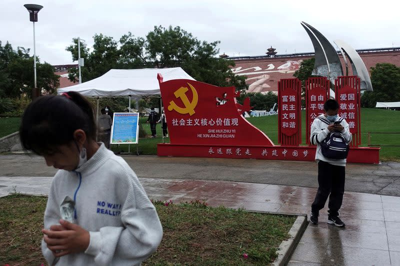 FILE PHOTO: Tourists stand in front of an installation promoting Chinese core socialist values with an emblem of Communist Party of China, in Beijing