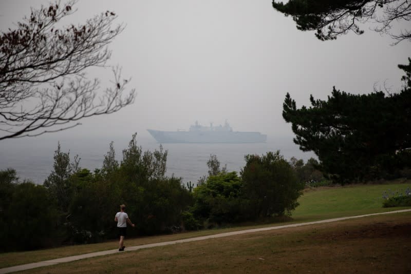 A man makes his way at the Eden Lookout as the Royal Australian Navy vessel HMAS Adelaide is covered by smoke in the town of Eden