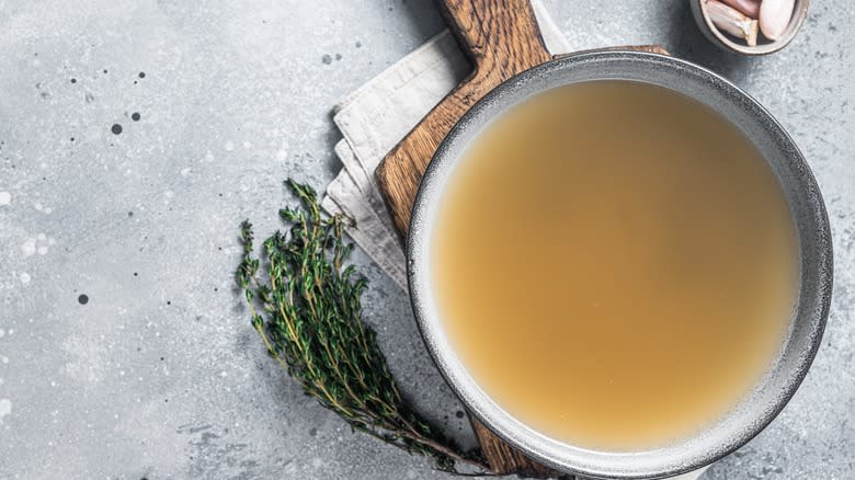 Beef broth in a bowl and herbs