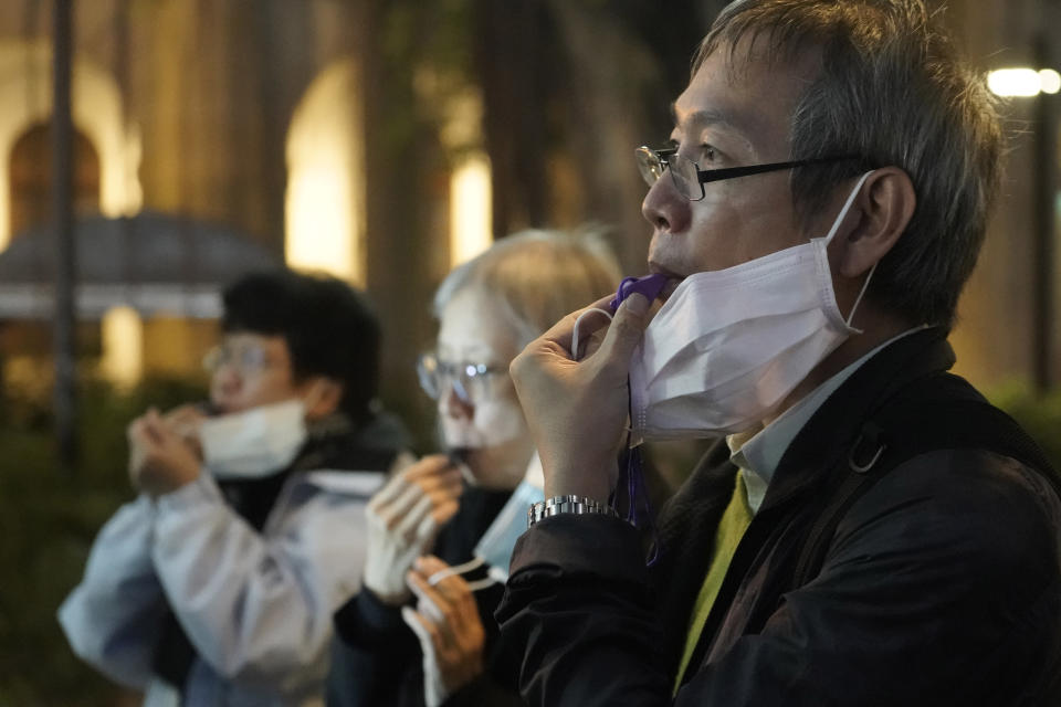 People with masks, blow whistles to representing whistleblower during a vigil for Chinese doctor Li Wenliang, in Hong Kong, Friday, Feb. 7, 2020. The death of a young doctor who was reprimanded for warning about China's new virus triggered an outpouring Friday of praise for him and fury that communist authorities put politics above public safety. (AP Photo/Kin Cheung)