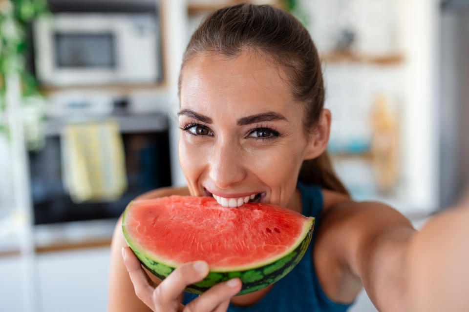 A photo of a young woman eats a slice of watermelon in the kitchen. 