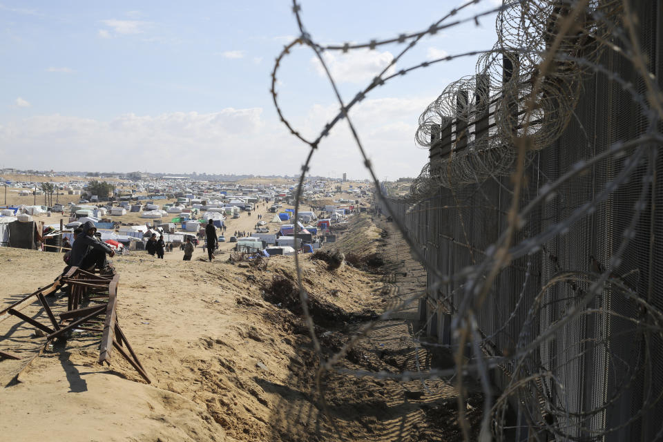 Palestinians displaced by the Israel air and ground offensive on the Gaza Strip sit next to the border fence with Egypt in Rafah, Wednesday, Jan. 24, 2024. (AP Photo/Hatem Ali)