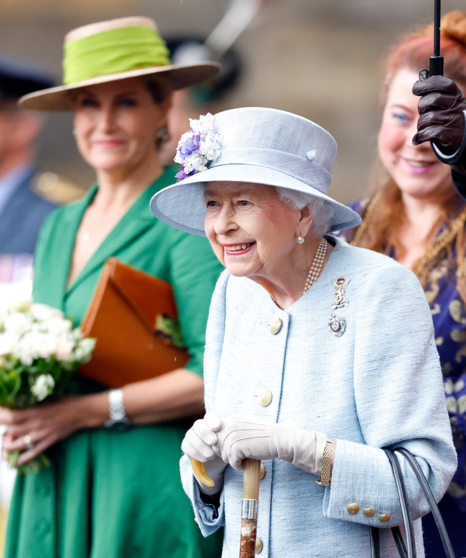 The Queen holding a walking stick and smiling. 