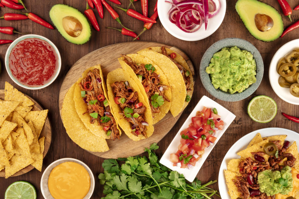 A photo of Mexican food, including tacos, guacamole, pico de gallo, nachos and others, shot from the top with ingredients on a dark rustic wooden background