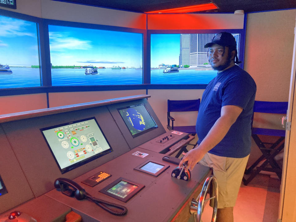 Davere Hanson, a Harbor School graduate who now serves as a teacher apprentice at the school, stands next to its beloved simulator. (Jo Napolitano)