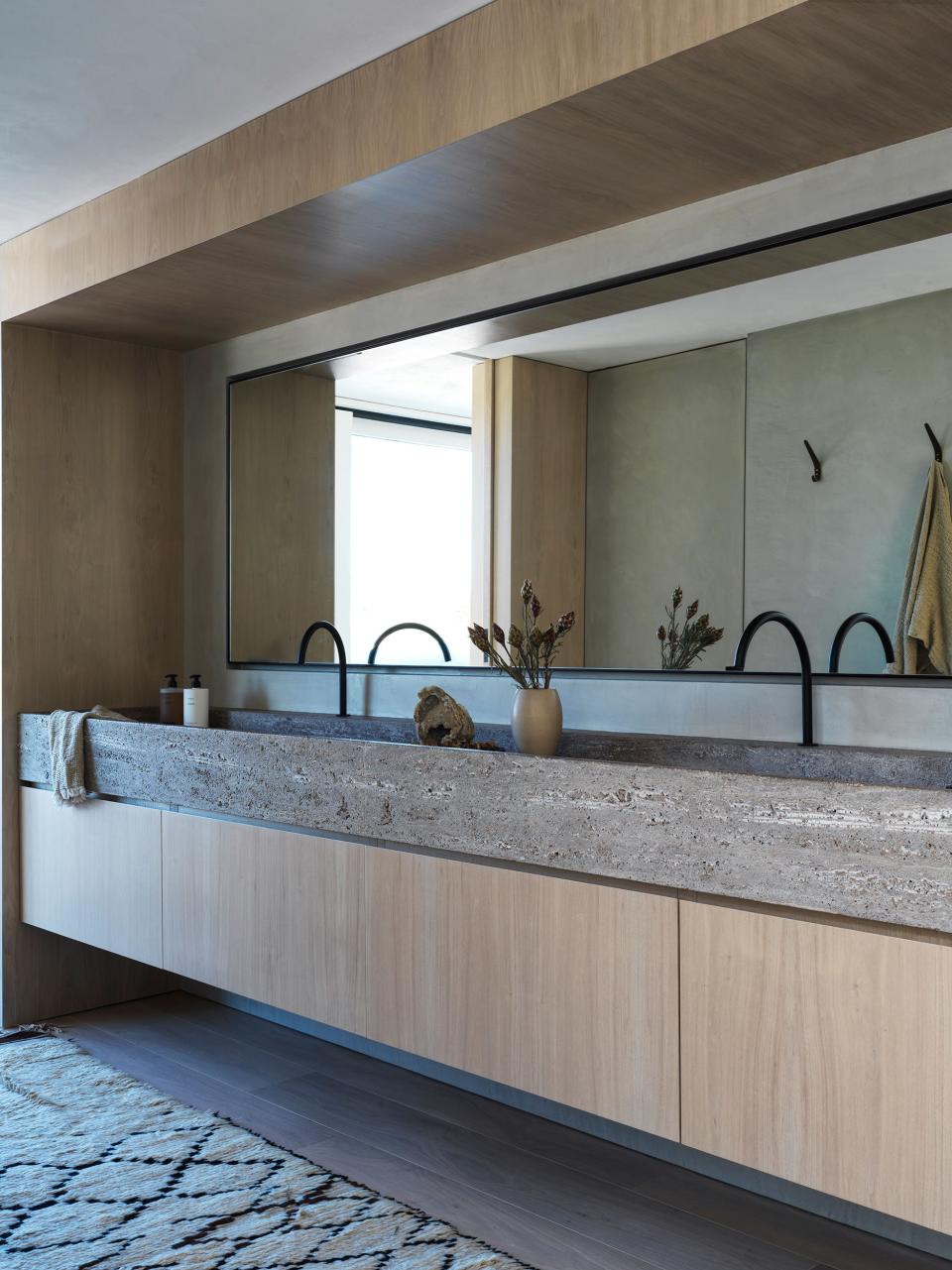 “The [primary] bathroom is really killer,” says Alexander of the well-lit space. The vanities are custom-designed by Alexander Design in bleached walnut with sandblasted titanium travertine, made by Vaselli and Cooritalia, with matte black plumbing by Vola and custom Cam Crawford mirror.