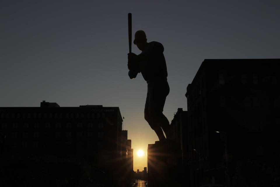 The sun sets in the distance as a statue of St. Louis Cardinals great Stan Musial stands outside a quiet Busch Stadium Friday, Aug. 7, 2020, in St. Louis. Major League Baseball announced Friday that a three-game series between the Chicago Cubs and Cardinals set for this weekend in St. Louis has been postponed after two more Cardinals players and a staff member tested positive for the coronavirus. (AP Photo/Jeff Roberson)