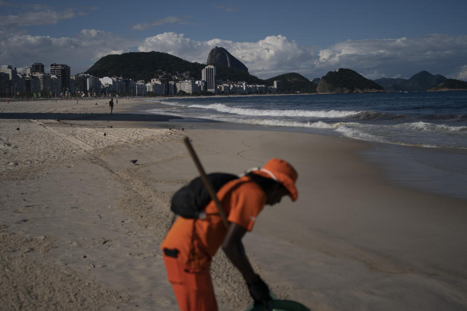 Gloria Maria cleans the shore of an unusually empty Copacabana beach backdropped by the Sugar Loaf Mountain in Rio de Janeiro, Brazil, Thursday, March 26, 2020, as people stay indoors to help contain the spread of the new coronavirus. The 41-year-old city worker said that in her 10 years of work cleaning the beach, she never saw an empty beach on a sunny Thursday. "It's terrible, people are dying in Europe due this virus," she added. (AP Photo/Leo Correa)