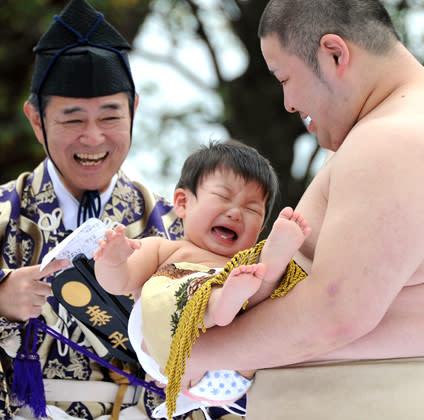 A student sumo wrestler carrys a crying baby beside a referee (L) clad in a traditional costume during the "Baby-cry Sumo" competition at Sensoji temple in Tokyo on April 21, 2012. Some 100 babies aged under one took part in the annual baby crying contest. Japanese parents believe that sumo wrestlers can help make babies cry out a wish to grow up with good health. AFP PHOTO/Toru YAMANAKA