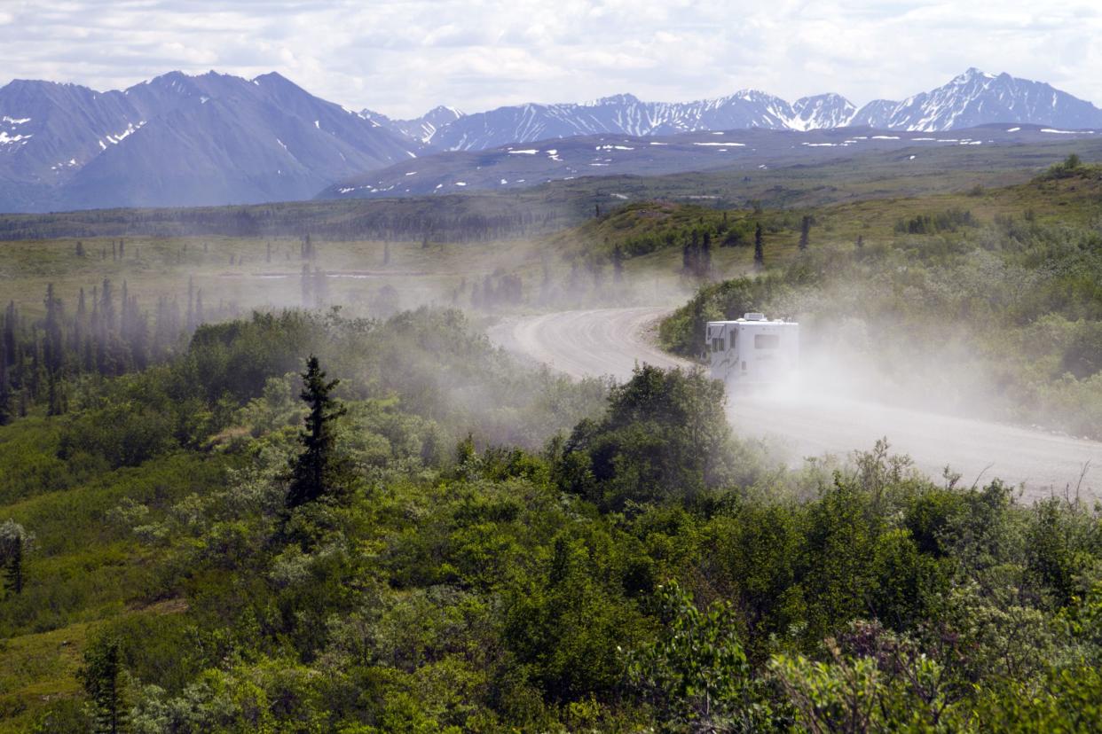 RV riding along gravel road in Denali National Park, dust from road with trees and mountain range in background