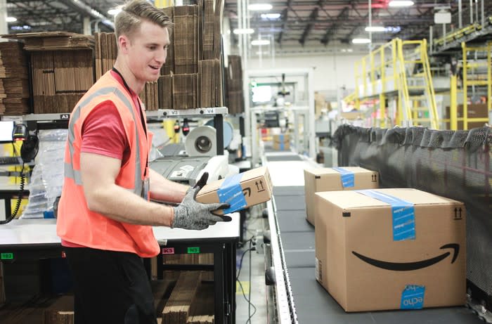 An Amazon warehouse worker placing a box on a conveyor belt.