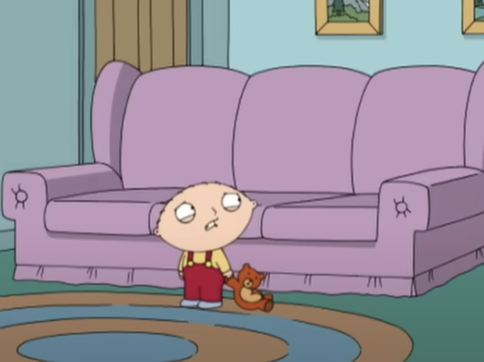 Animated character Stewie Griffin from Family Guy sitting on the floor with a teddy bear beside him