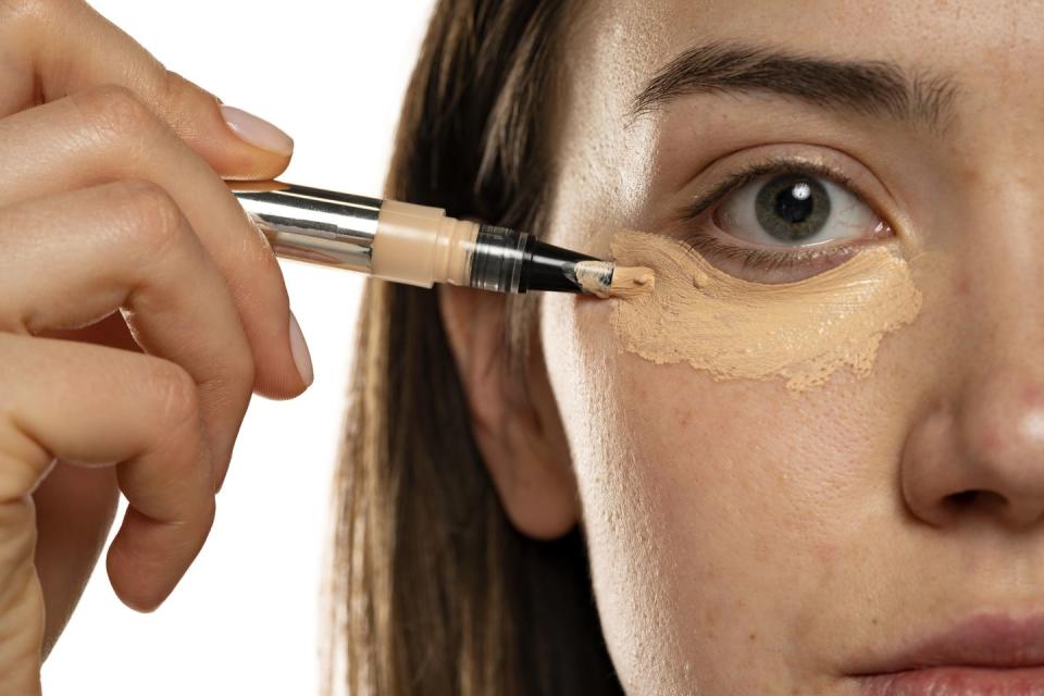 close up of a young women applying concealer under her eyes