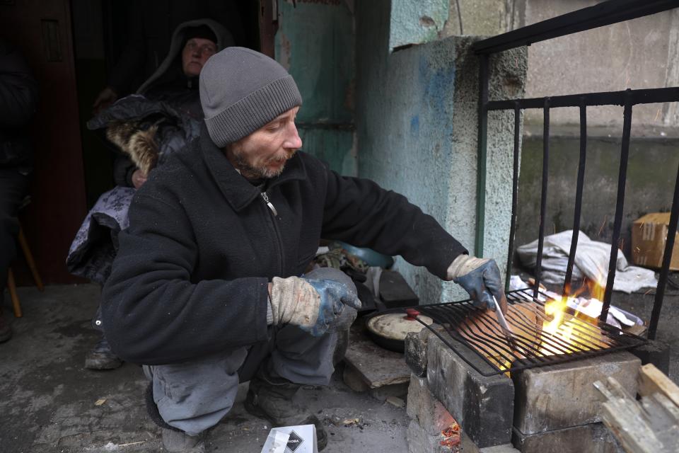 A local resident prepares to cook at an entrance of a building damaged during fighting in Mariupol, in an area that Russian-backed separatists claim to control in the Ukraine city of Mariupol, Wednesday, April 13, 2022.(AP Photo/Alexei Alexandrov)