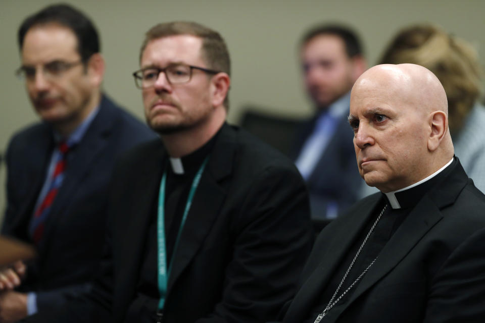 FILE - In this Feb. 19, 2019, file photo, from front to back, Samuel Aquila, archbishop of the Denver diocese of the Roman Catholic Church, Very Rev. Randy Dollins, vicar general, and Colorado Attorney General Phil Weiser listen about the plan to have a former federal prosecutor review the sexual abuse files of Colorado's Roman Catholic dioceses at a news conference in Denver. Nine more Catholic priests, including one well known for helping Denver's homeless, have been identified as sexually abusing children in Colorado in a follow-up report released Tuesday, Dec. 1, 2020, by Weiser. (AP Photo/David Zalubowski, File)