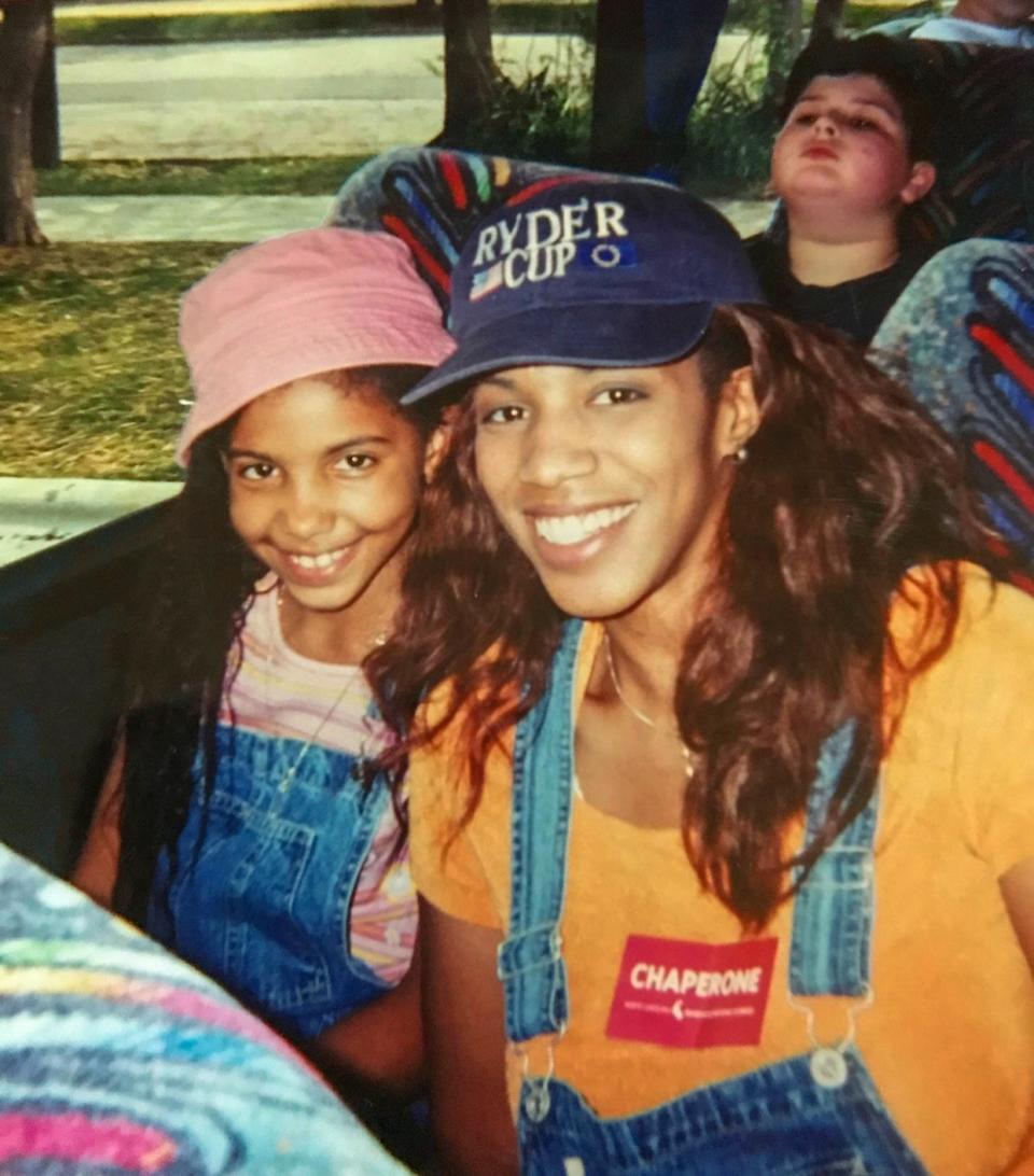 A young Cheslie and April, both in overalls and hatted, seated on a bus during a school field trip in the early 2000s. 