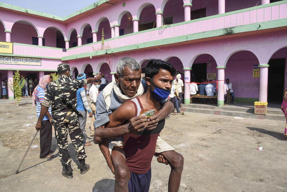 A young man carrying his father leaves after they cast their votes for the first phase of Bihar Assembly Elections, at Paliganj constituency in Patna, Wednesday, 28 October.