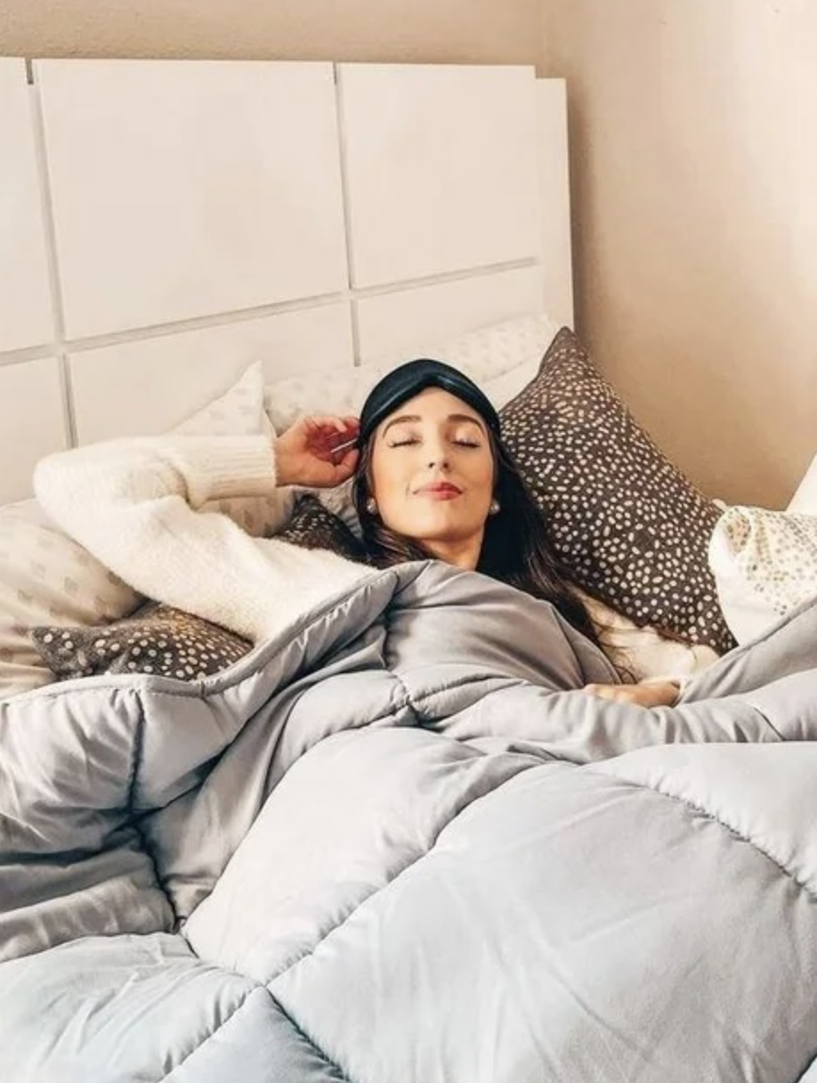 A model wearing a black cushioned sleep mask while lying in bed