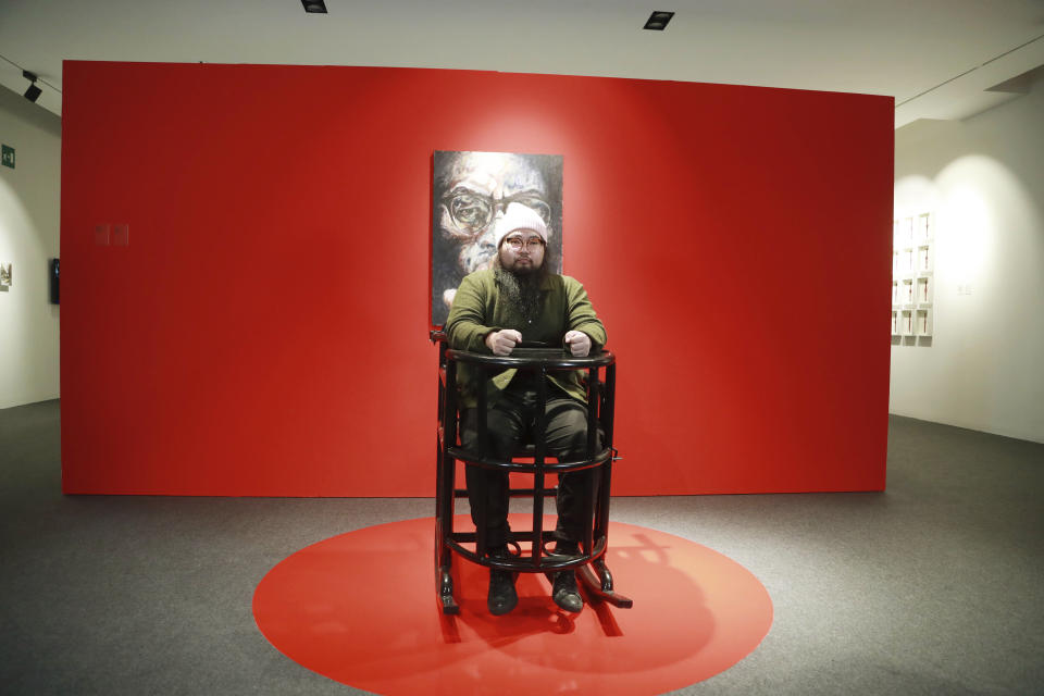 Artist Badiucao sits in a torture chair, part of his exhibition in the Santa Giulia Museum, in Brescia, Saturday, Nov. 13, 2021. A provocative exhibit by dissident Chinese artist Badiucao opened Saturday in the industrial northern Italian city of Brescia despite pressure from the Chinese embassy in Rome to cancel it. A letter from the embassy included veiled economic threats, noting Italy’s trade with China, in a bid to prevent the first solo exhibit by Badiucao — the pseudonym used by the artist whose work takes aim at China's policies and human rights record. During the exhibit’s opening days, Badiucao will sit in a torture chair and read from a diary shared with him by a resident of Wuhan, the Chinese city where the coronavirus was first detected. (AP Photo/Felice Calabro')