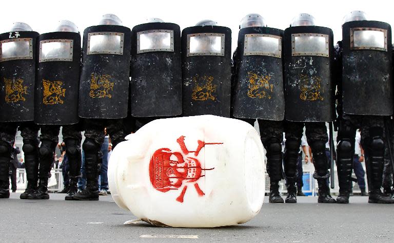 Riot policemen stand in front of a plastic barrel --representing farm pesticides-- thrown by members of the Landless Rural Workers Movement during a protest in Brasilia, on February 12, 2014