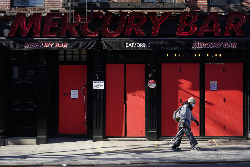 A pedestrian walks past a boarded-up bar, Sunday, Jan. 10, 2021, in the Hell's Kitchen neighborhood of New York. The boarded-up windows and For Rent signs are all over the place in Manhattan’s Hell’s Kitchen neighborhood. Nearby, the Broadway theaters are all dark. But the economic darkness brought on by the coronavirus pandemic has had a few bright spots. A couple of well-loved venues have gotten financial boosts, thanks to online fundraising campaigns and even a telethon. (AP Photo/Mary Altaffer)