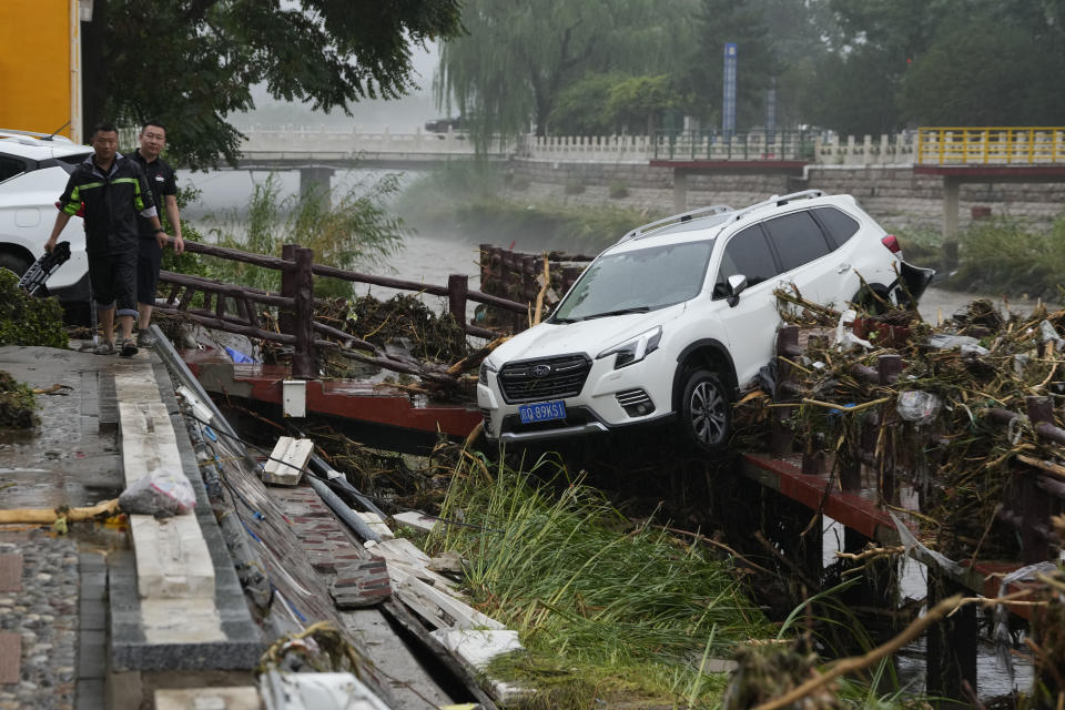Residents walk near a vehicle washed away by flood waters in the Mentougou district on the outskirts of Beijing, Tuesday, Aug. 1, 2023. Chinese state media report some have died and others are missing amid flooding in the mountains surrounding the capital Beijing. (AP Photo/Ng Han Guan)
