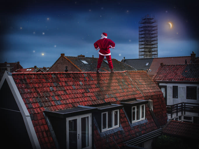 Night scene with the moon. Successful Santa Claus stands on the roof of an old house with his hands on his hips.