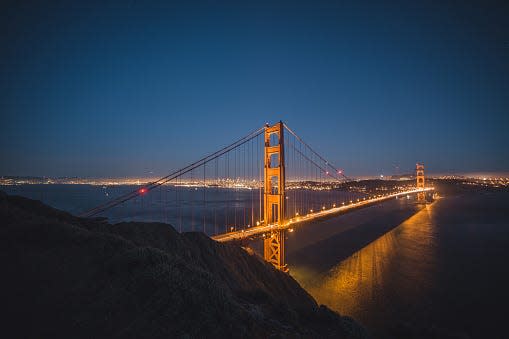 Light trails on illuminated Golden Gate Bridge at night with city skyline at background, San Francisco, California, USA.