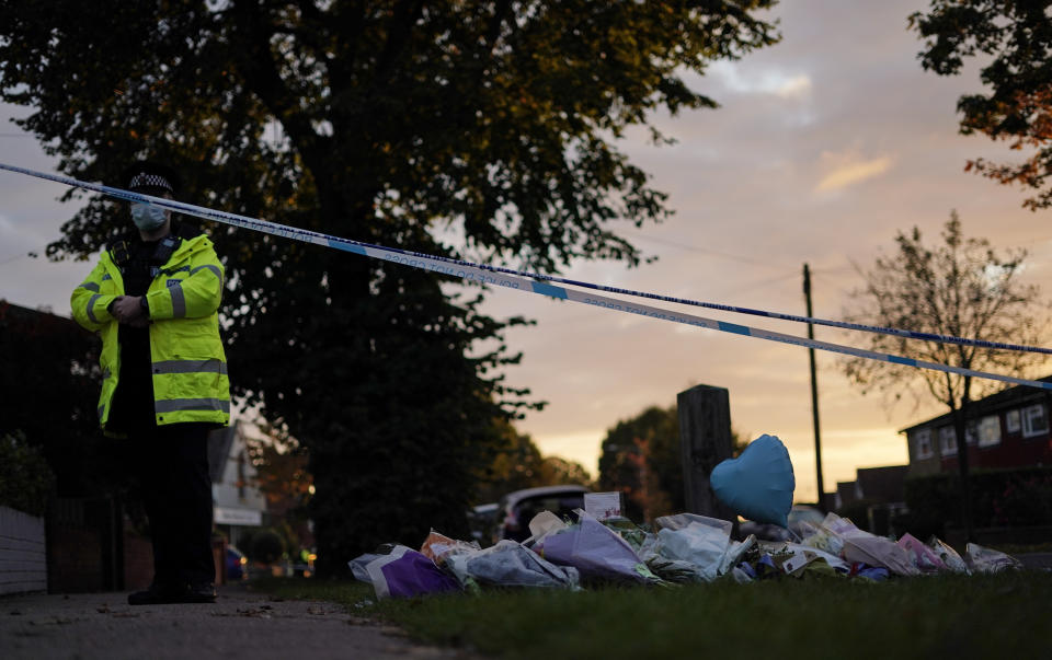 A police officer stands near floral tributes placed near the Belfairs Methodist Church in Eastwood Road North, in Leigh-on-Sea, Essex, England, Saturday, Oct. 16, 2021 where British Conservative lawmaker David Amess died after being stabbed at a constituency surgery on Friday. Amess, a long-serving member of Parliament was stabbed to death during a meeting with constituents at a church in England, in what police said was a terrorist incident. A 25-year-old man was arrested in connection with the attack, which united Britain's fractious politicians in shock and sorrow. (AP Photo/Alberto Pezzali)