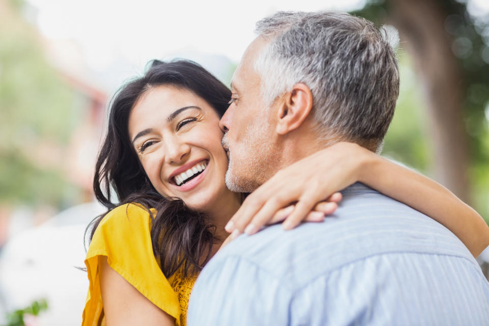 Man kisses woman’s cheek as she smiles, embracing each other