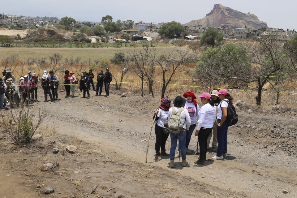 Women holding digging tools stand at the site where they said they found a clandestine crematorium, as the press and police stand by in Tlahuac, on the edge of Mexico City, Wednesday, May 1, 2024. A leader of one of the groups of so-called "searching mothers" from northern Mexico, announced late Tuesday that her team had found bones around clandestine burial pits and ID cards, and prosecutors said they were investigating to determine the nature of the remains. (AP Photo/Ginnette Riquelme)