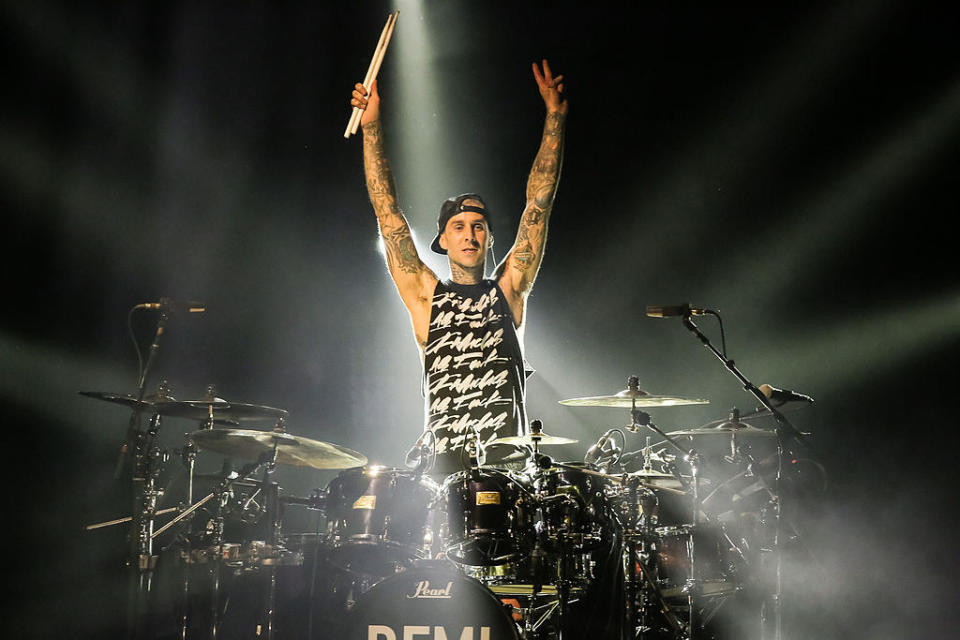 Travis standing behind a drum set with his arms raised