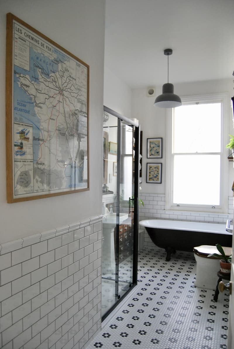 Map of Paris framed ina a bathroom with a glass shower and black tub.