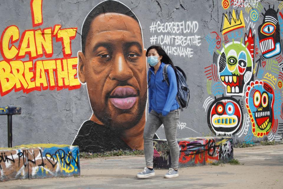 A woman wearing a protective mask walks past a graffiti depicting a portrait of George Floyd, a black man who died in Minneapolis after a white policeman kneeled on his neck for several minutes is seen in Berlin's Mauer Park on May 30, 2020. (Photo by Odd ANDERSEN / AFP) (Photo by ODD ANDERSEN/AFP via Getty Images)