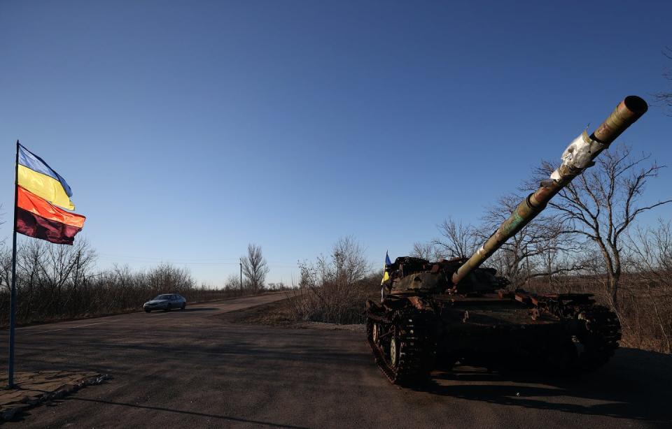 A tank sits by the side of an open road with a flag visible.