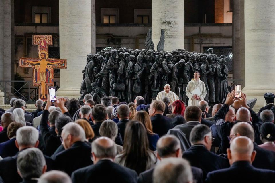 Pope Francis leads a prayer for migrants and refugees, part of the 16th general assembly of the synod of bishops, in front of Timothy Schmalz's bronze sculptural complex 'Angels Unawares' and the San Damiano Cross, left, a large Romanesque rood before which St. Francis of Assisi was praying when he is said to have received the commission from the Lord to rebuild the Church, in St. Peter's Square at The Vatican, Thursday, Oct. 19, 2023. (AP Photo/Gregorio Borgia)