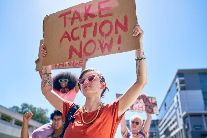 A group of people holding protest signs that read "Take Action Now!," "Change," and "Equal Rights" at a street demonstration