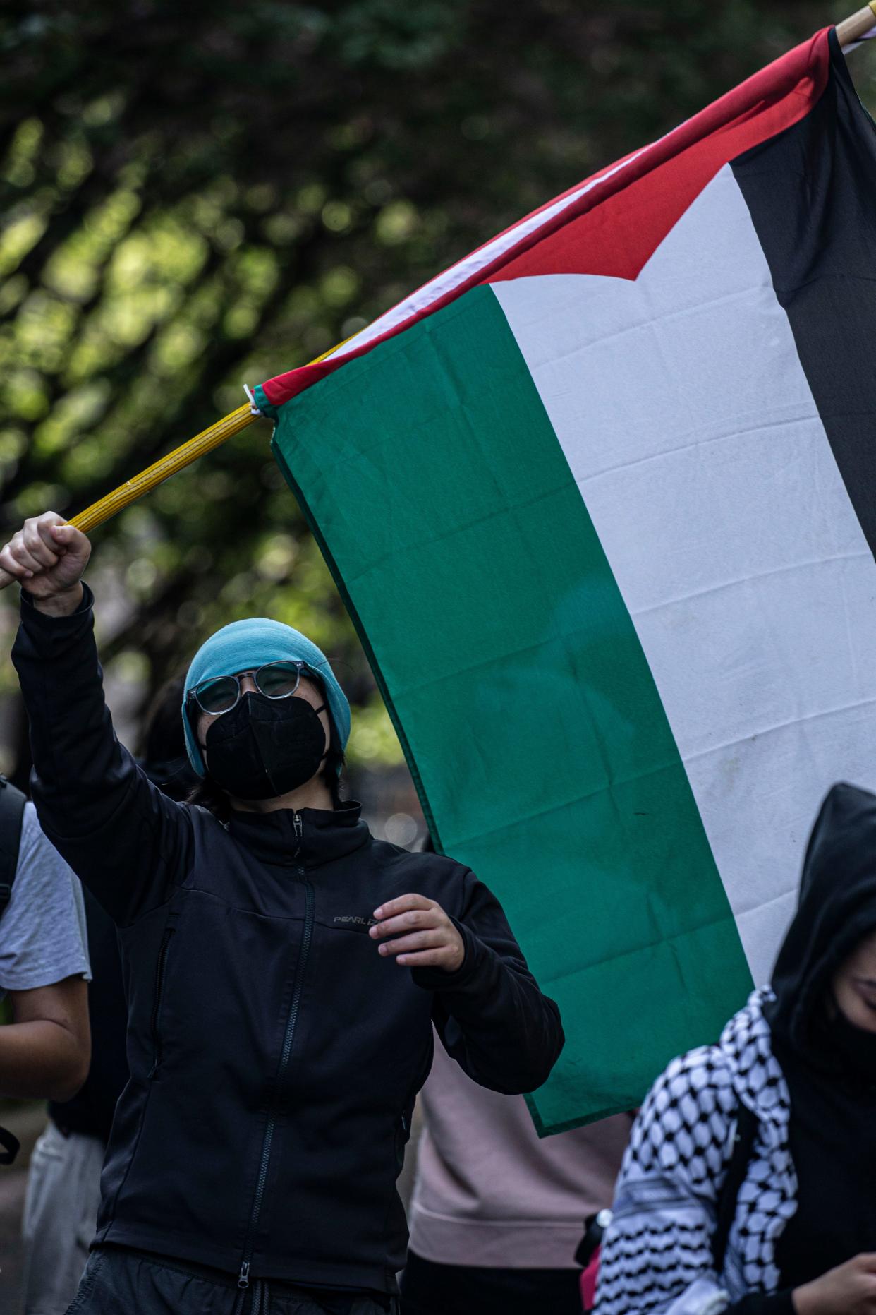 A student protester waves a Palestinian flag from inside the gates of Columbia University April 30, 2024 as hundreds protested on the sidewalk outside the campus gates.